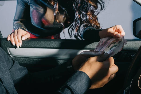 Vista recortada del cliente en coche dando dinero en efectivo a la prostituta - foto de stock