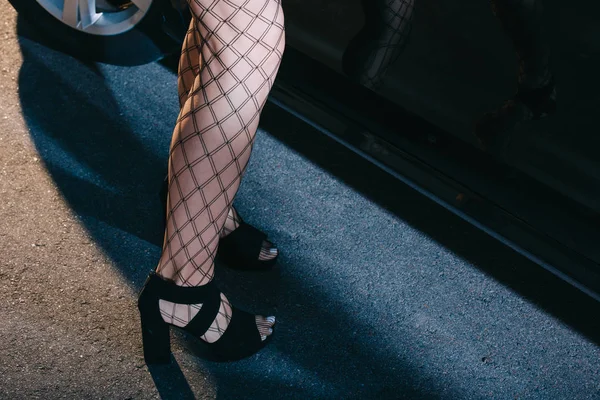 Обрезанный вид женщины в сетчатых чулках, стоящей в обуви рядом с машиной — стоковое фото