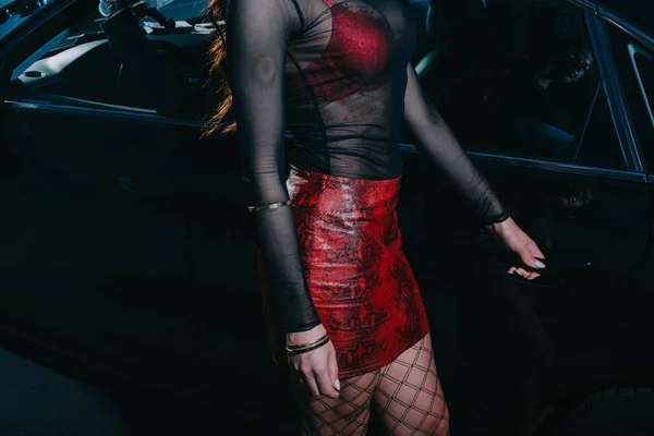 Обрезанный вид проститутки в красной юбке, стоящей возле черного авто — стоковое фото
