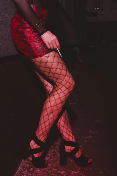 Vista ritagliata della donna in gonna rossa in piedi vicino al muro e con la sigaretta in mano — Foto stock