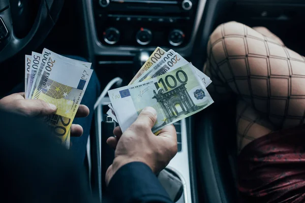 Vista recortada del cliente pagando billetes en euros a prostituta en coche - foto de stock