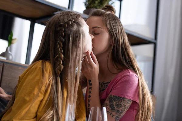 Two lesbians with wine glass kissing in living room — Stock Photo