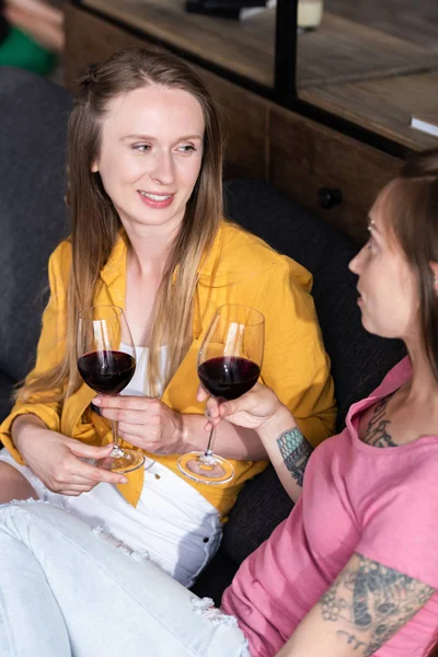 Two lesbians holding wine glasses while sitting on sofa in living room — Stock Photo