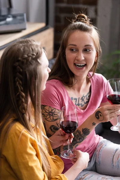 Duas lésbicas segurando copos de vinho enquanto sentado no sofá na sala de estar — Fotografia de Stock