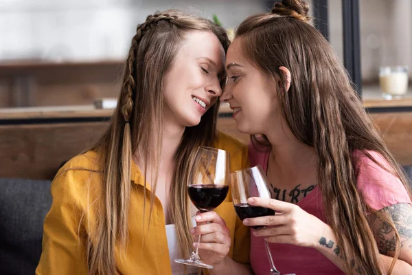 Dos lesbianas sosteniendo copas de vino mientras están sentadas en el sofá en la sala de estar - foto de stock