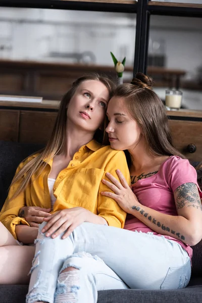 Two pretty lesbians embracing while sitting on sofa in living room — Stock Photo