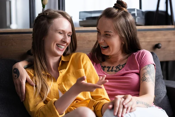 Zwei hübsche Lesben umarmen sich, während sie auf dem Sofa im Wohnzimmer sitzen — Stockfoto