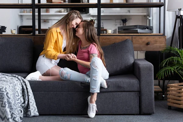Two smiling lesbians holding hands while sitting on sofa in living room — Stock Photo