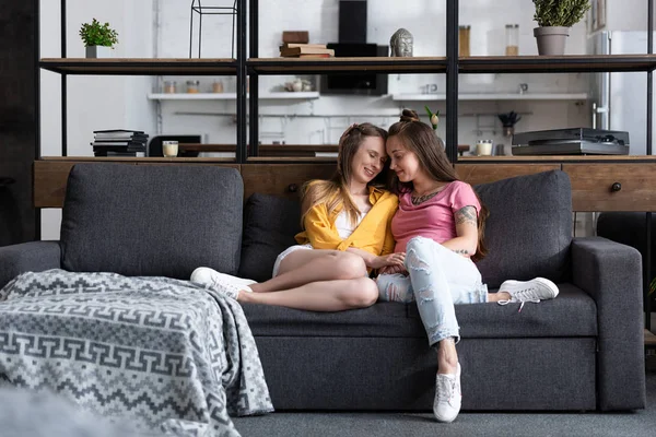 Two smiling lesbians holding hands while sitting on sofa in living room — Stock Photo