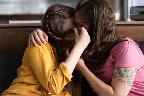 Due lesbiche che coprono i volti con i capelli abbracciando e baciando in soggiorno — Foto stock
