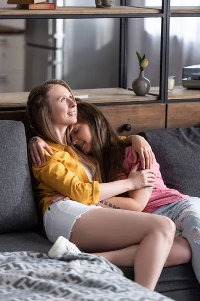 Dos hermosas lesbianas abrazando mientras se sienta en el sofá en la sala de estar - foto de stock