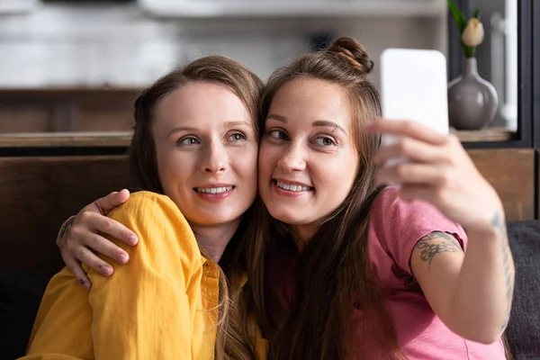 Dos lesbianas abrazando mientras toma selfie en casa - foto de stock