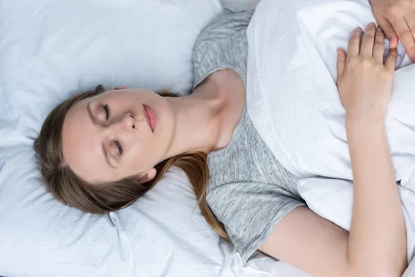 Вид сверху на молодую женщину, спящую в кровати под одеялом — стоковое фото