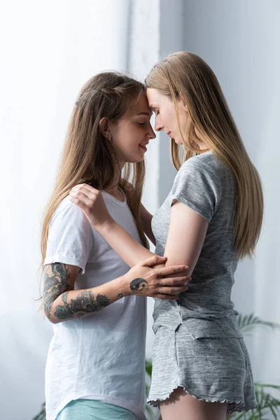 Duas lésbicas sorridentes em camisetas abraçando no quarto — Fotografia de Stock