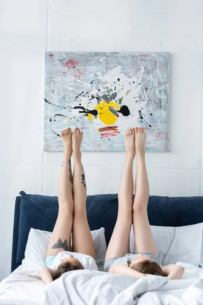 Two barefoot lesbians lying on bed with legs up in morning — Stock Photo