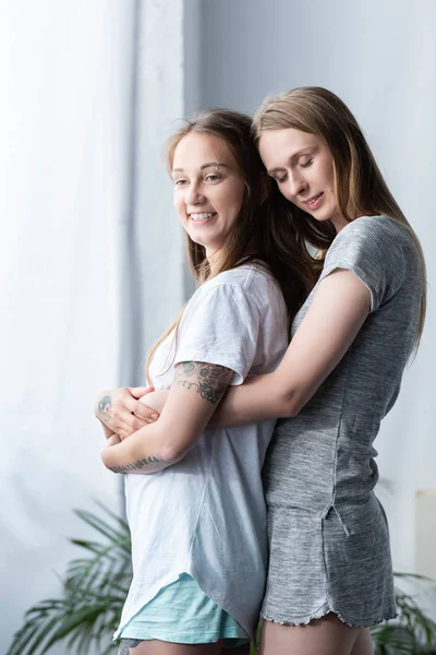 Two smiling lesbians in t-shirts embracing in bedroom — Stock Photo
