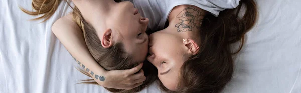 Panoramic shot of two lesbians embracing and kissing on bed — Stock Photo