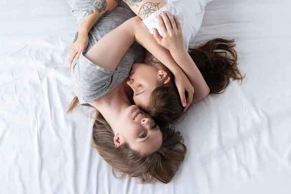 Верхний вид двух улыбающихся лесбиянок, обнимающихся, лежа на кровати — стоковое фото