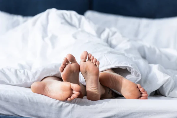 Vue partielle de deux lesbiennes pieds nus couchées sous la couverture — Photo de stock