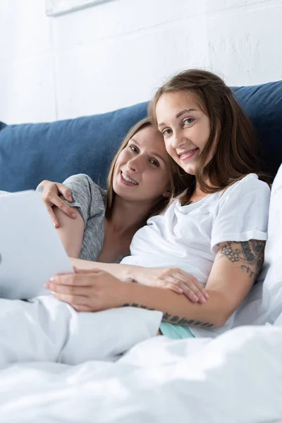 Zwei lächelnde Lesben, die sich umarmen, während sie morgens Laptop im Bett benutzen — Stockfoto