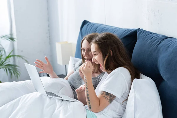 Duas lésbicas excitadas sorridentes usando laptop na cama de manhã — Fotografia de Stock