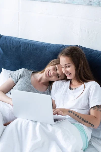 Due lesbiche sorridenti che si abbracciano mentre usano il computer portatile a letto al mattino — Foto stock