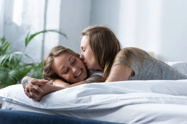 Two lesbians holding hands and kissing while lying on bed in morning — Stock Photo
