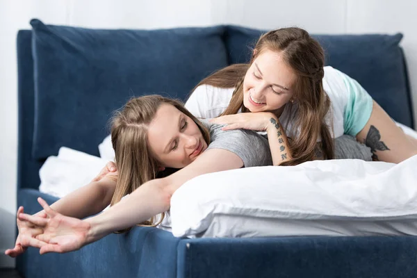 Dos lesbianas sonrientes tumbadas en la cama por la mañana en el dormitorio - foto de stock