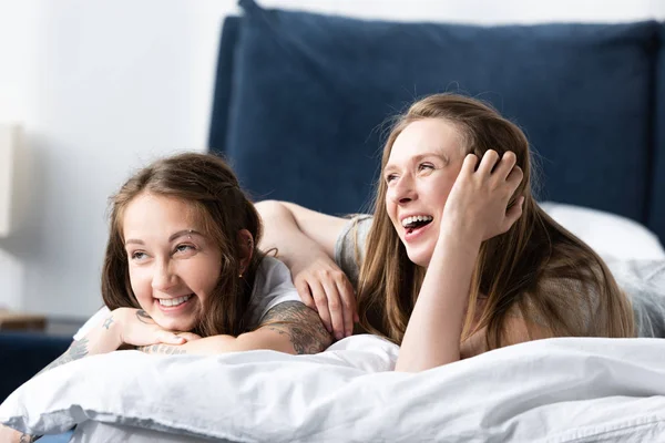 Two laughing lesbians lying on bed in morning in bedroom — Stock Photo