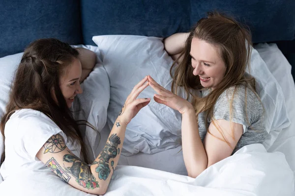 Duas lésbicas sorridentes tocando as mãos e olhando um para o outro na cama — Fotografia de Stock