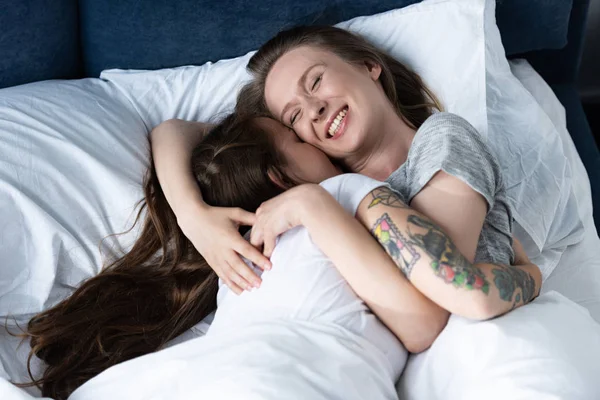 Dos lesbianas sonrientes abrazándose mientras yacen en la cama - foto de stock