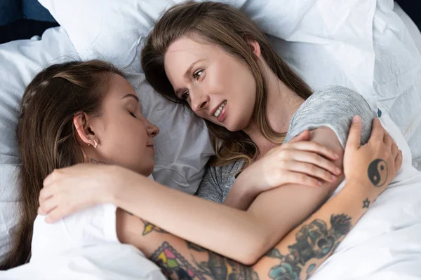 Dos lesbianas sonrientes abrazándose mientras yacen en la cama - foto de stock