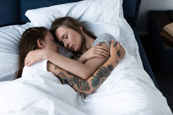 Dos lesbianas abrazándose mientras duermen debajo de una manta en la cama - foto de stock