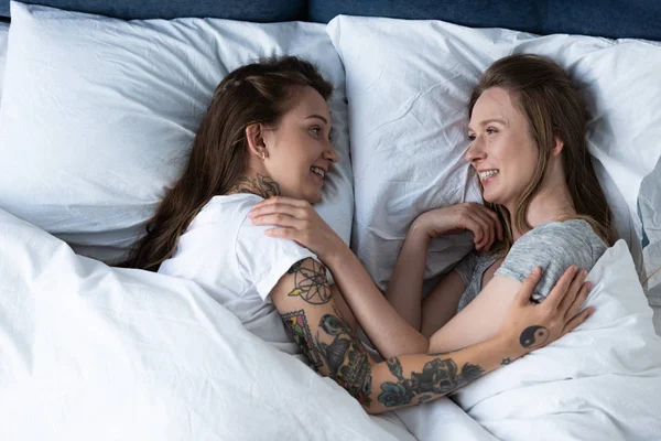 Две улыбающиеся лесбиянки обнимаются, лежа в постели — стоковое фото
