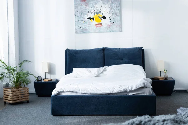 Уютная современная спальня с кроватью и зеленым растением — стоковое фото