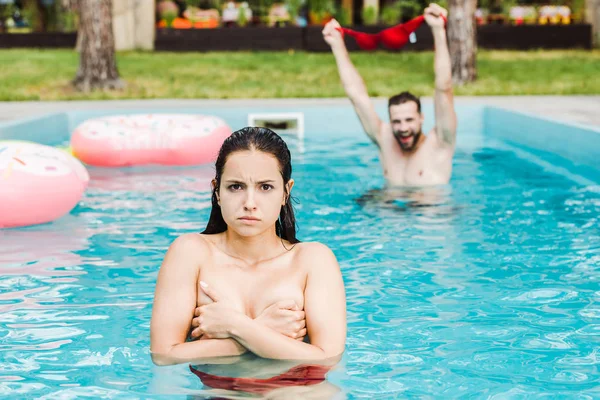 Foco seletivo da mulher cobrindo seios na piscina perto do homem — Fotografia de Stock
