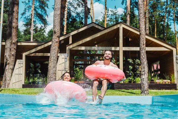 Happy man and woman with inflatable rings jumping in swimming pool — Stock Photo