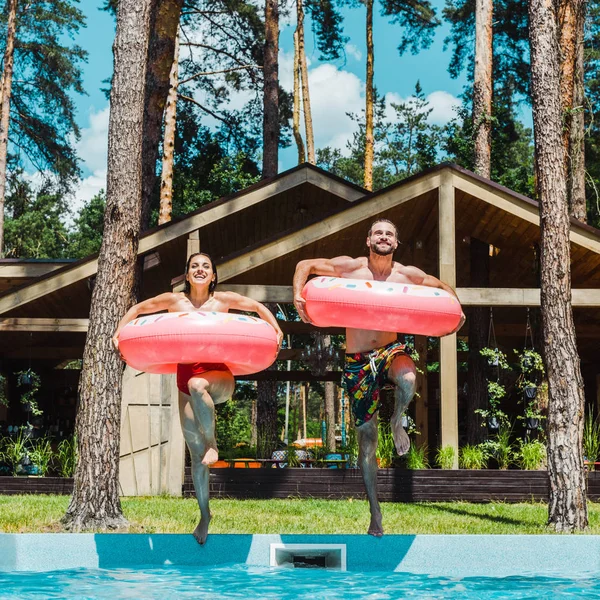 Cheerful woman and man with inflatable rings jumping in swimming pool — Stock Photo