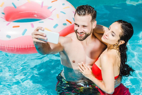 Overhead view of bearded shirtless man taking selfie on smartphone near attractive woman — Stock Photo