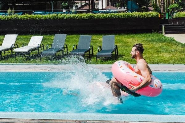 Side view of man with inflatable ring jumping in swimming pool — Stock Photo