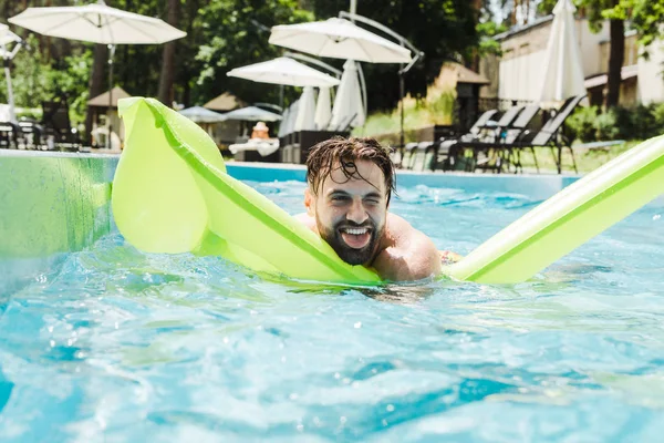 Uomo che nuota con materasso gonfiabile mostrando la lingua in piscina — Foto stock