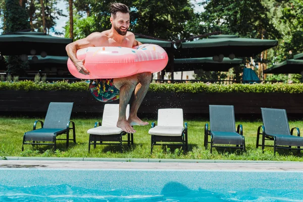 Homem barbudo feliz com salto descalço na água ao segurar o anel inflável — Fotografia de Stock