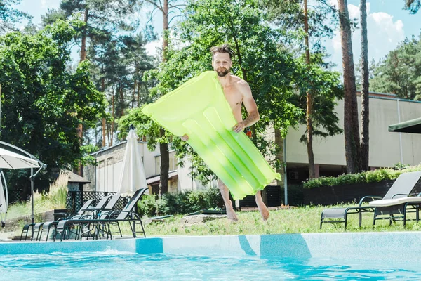 Homme barbu heureux avec pieds nus sautant dans l'eau tout en tenant matelas gonflable — Photo de stock