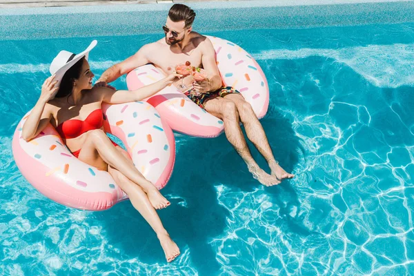 Blick von oben auf eine fröhliche Frau mit Strohhut, die mit einem gutaussehenden Mann Cocktailgläser klappert — Stockfoto