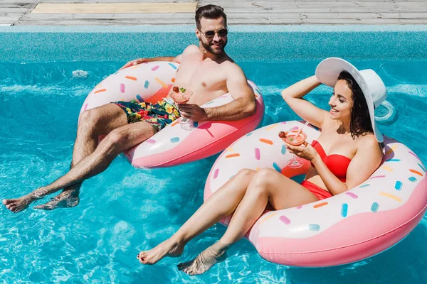 Chica feliz en sombrero de paja y hombre guapo sosteniendo vasos de cóctel — Stock Photo