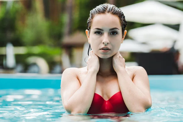 Attractive brunette young woman touching neck and looking at camera in swimming pool — Stock Photo