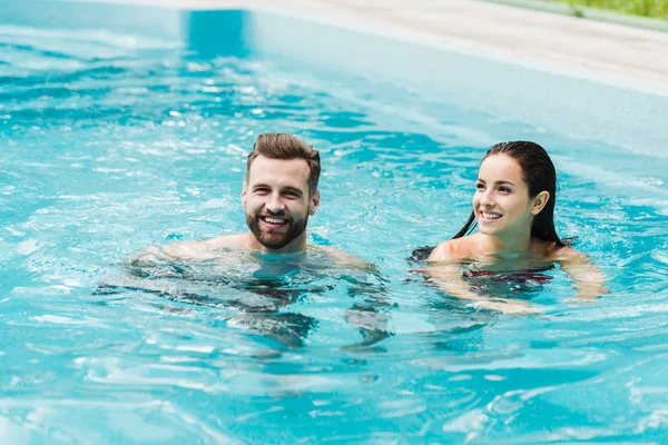 Bonito barbudo homem sorrindo perto atraente mulher no piscina — Fotografia de Stock