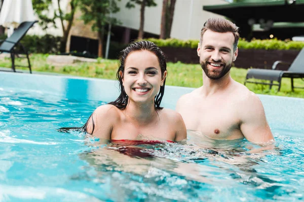 Foco seletivo de homem barbudo bonito sorrindo perto de mulher atraente na piscina — Fotografia de Stock