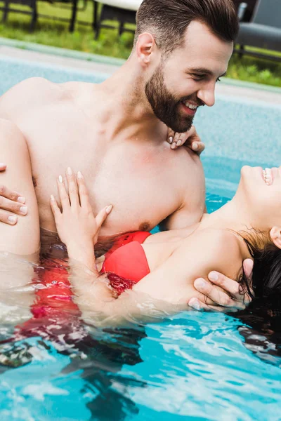 Hombre barbudo guapo mirando a la mujer joven sonriendo en la piscina - foto de stock