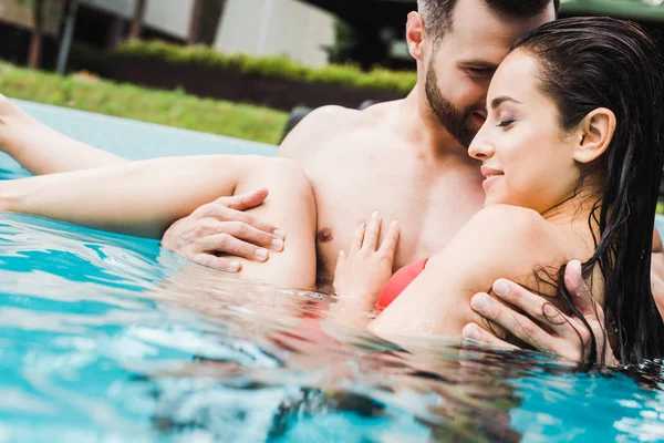 Enfoque selectivo de hombre barbudo guapo y mujer joven sonriendo en la piscina - foto de stock